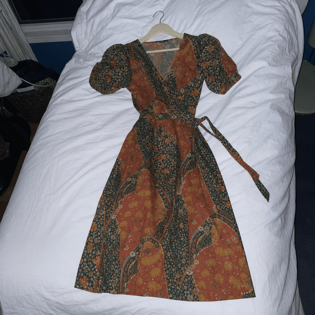 A printed wrap dress photographed on a bed at night under a ceiling light